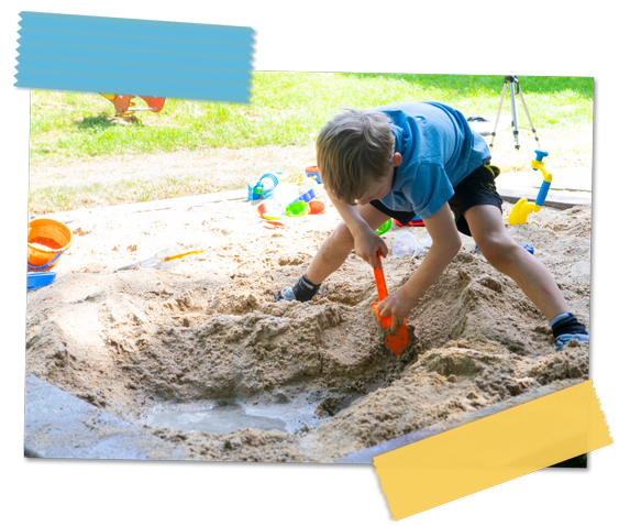 Ein Junge buddelt mit einer orangen Schaufel ein Loch im Sandkasten,