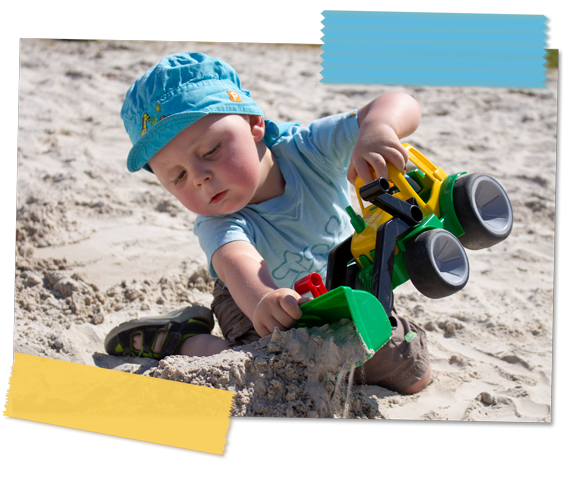 Kleinkind mit Sand-Traktor, das einen Sandhügel aufschüttet