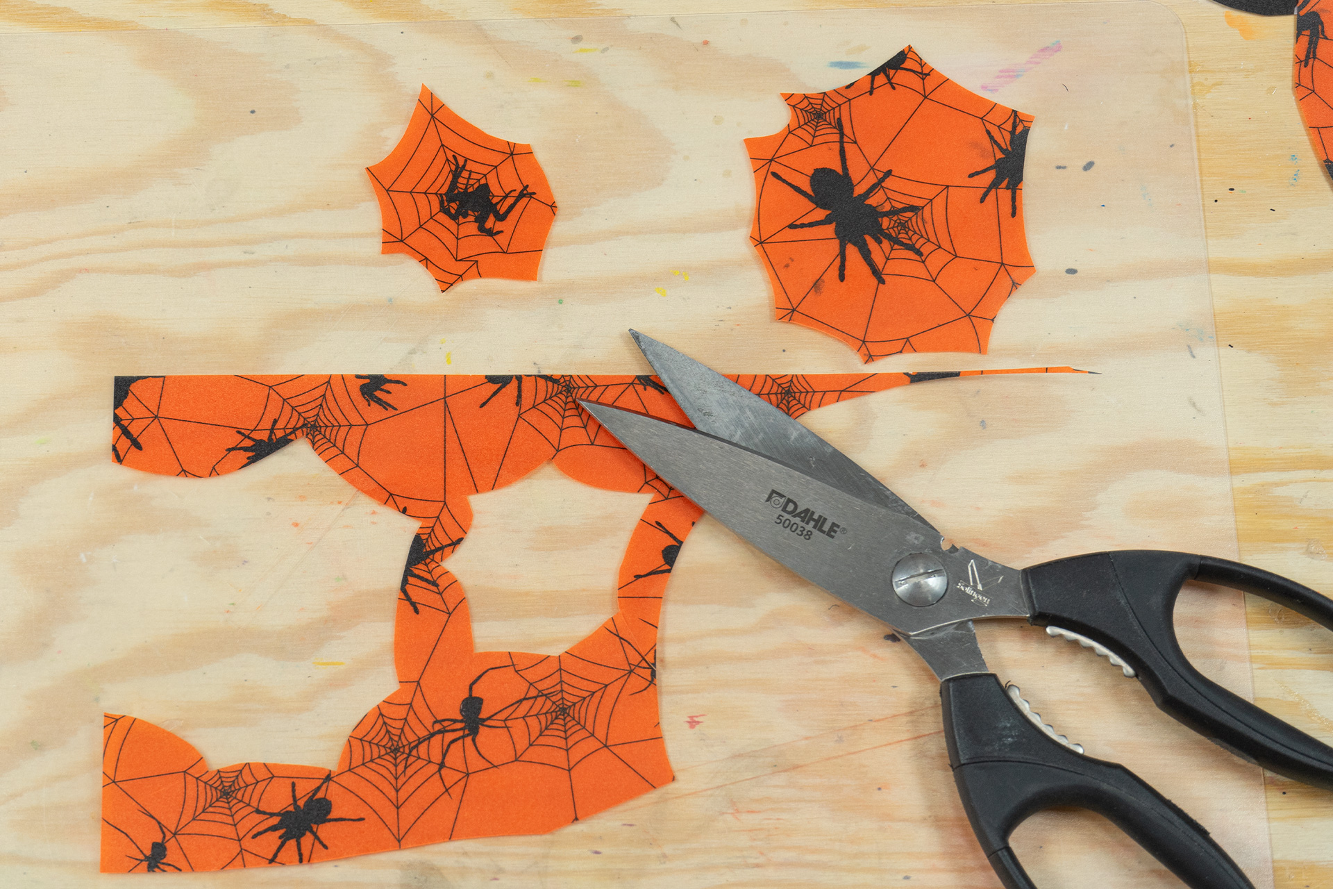 <p>Aus dem orangenfarbenen Spinnennetz-Transparentpapier schneide ich kleine Spinnennetze und bringe diese als zusätzliche De