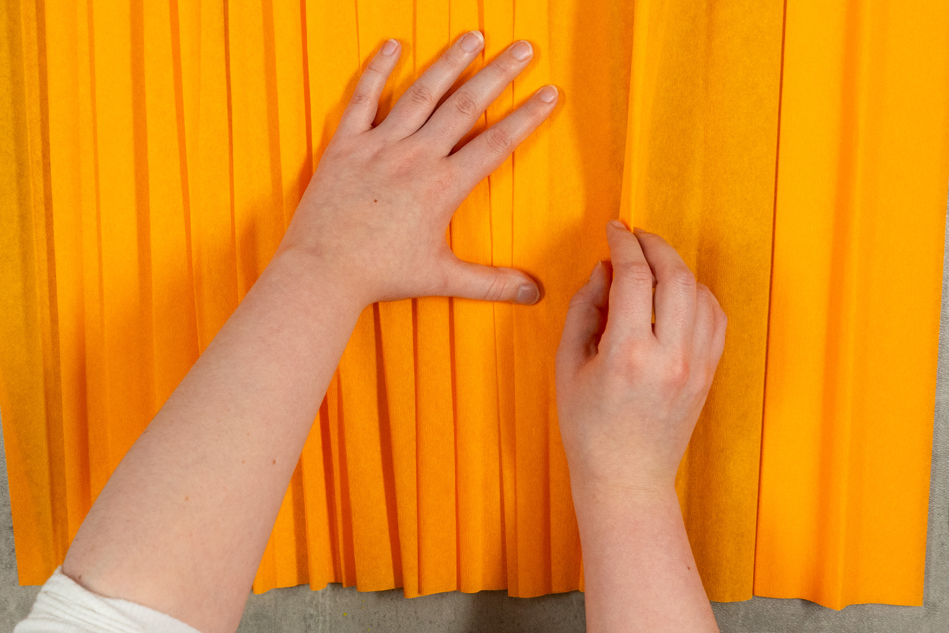 <p>Ich nehme mir das orangefarbene Krepppapier zur Hand und lege es in lockere Falten.</p>