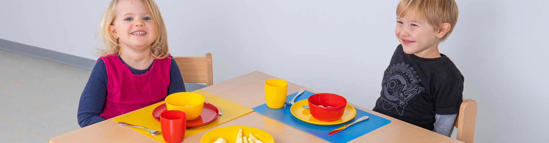 Kindergeschirr aus Porzellan  oder Kunststoff - Mädchen und Junge sitzen am Tisch 